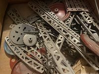 Assorted metal parts of the vintage toy construction set including perforated metal strips, wheels, pulleys, and connectors, displayed in detail.