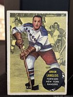 Front of a 1961-62 Topps hockey card featuring Junior Langlois in New York Rangers uniform, posed with hockey stick.