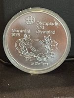 Front side of coin with Olympic rings, Montreal 1976 markings, denomination and wreath.