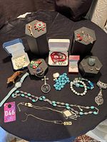 Photo showing entire jewelry lot spread on a black surface with various rings, bracelets, necklaces, brooches, watch, and earrings.