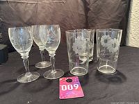 Photo showing three stemmed wine glasses and two tall drinking glasses with etched Hughes Cornflower floral pattern.