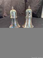 Pair of vintage silverplate sugar shakers shown front view with flared bases and perforated lids with pointed finials.
