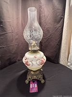 Full front view of the vintage antique kerosene lantern showing hand-painted floral designs on the white glass reservoir and tall etched glass chimney.