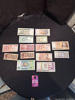 Collection of 14 assorted world paper money banknotes arranged on a black surface showing various designs and denominations.