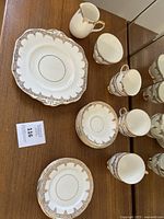 Photo showing part of the set: cream pitcher, sugar bowl, teacups, saucers, and dessert plates clustered together, showing detailed floral gold trim borders on white porcelain.