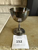 Silver cup on carpet floor with auction tag, showing cup shape and condition.