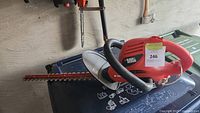 Electric Black & Decker hedge trimmer laying flat, showing the blade length and design with red and black color scheme.