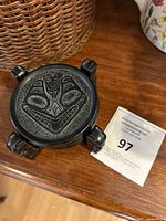 Top view of a single black coaster with a carved bear face design in Inuit style, showing details of the mask.