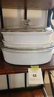 Three stacked white Corning Ware casserole dishes, two with clear glass lids, one lid missing