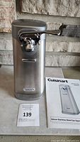 Front view of the Cuisinart stainless steel can opener with instruction booklet and auction tag 139.