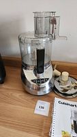 Food processor assembled with bowl, lid, and pusher on wood surface, showing front controls and Cuisinart logo on stainless steel base.