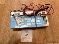 Top-down view of Beckman digital multimeter, probes coiled and secured on top, manual partially visible.