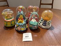 Photo showing six snow globes arranged on table, including Care Bear and various Disney character globes.
