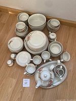 Full set photo showing all pieces including plates, bowls, cups, teapot, sugar bowl, creamer, salt and pepper shakers, and serving trays arranged on wooden floor.