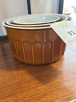 Three nesting ceramic bowls stacked one inside the other on a wooden surface, showing the brown exterior with embossed vertical pattern.