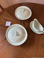 Two covered serving bowls with lids and a gravy boat on a wooden table.