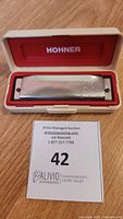 Hohner harmonica inside open cream plastic case with red lining, brand name visible inside case lid