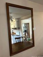 Front view of large rectangular mirror showing wooden frame and reflection of kitchen and dining area.
