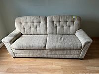Full front view of the beige fabric loveseat couch showing the tufted backrest and overall shape.