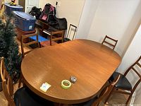Oval teak dining table with multiple teak chairs featuring black vinyl seats