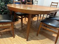 View of oval teak tabletop with four tapered legs and surrounding chairs