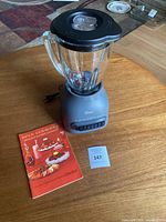 Oster electric blender on wooden table with recipe book and lot number card.