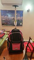Front view of pink and black Ogio rolling backpack with telescopic handle on display indoors
