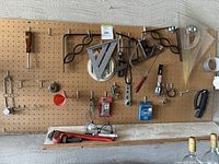Wide view of pegboard with various hand tools including measuring squares, pipe wrench, clamps, brushes and small tools.