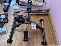 Photo of under desk pedal exercise machine showing the frame, pedals, and digital display on a wooden floor.