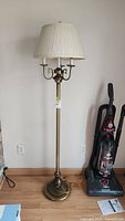 Full height view of the vintage brass floor lamp with four bulbs and white pleated shade showing its overall condition and design.