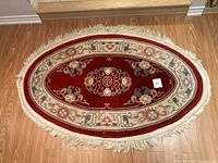 Full view of vintage oval rug on wooden floor showing overall design and fringed edges.