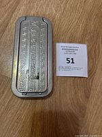 Metal razor sharpener inside decorative metal case with geometric pattern on lid, photographed on a wooden floor alongside an auction lot marker