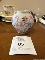 Vintage small ginger jar with pink bird and floral decoration on side, shown on wooden table with other crockery near it, front view.