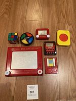 Photo showing six vintage toys including Rubik's Cube, Etch A Sketch, Simon Says, and other toys arranged on a floor.