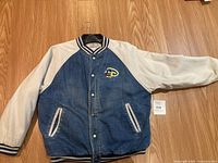 Full front view of the vintage Disney denim bomber jacket laid flat showing denim body and white sleeves with striped collar and cuffs.