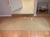 Full view of the beige woven rectangular rug placed on a wood floor in front of tiled threshold.
