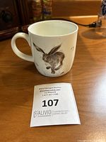 Side view of the mug featuring a brown and grey hare mid-jump illustration on a white background.