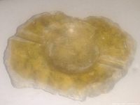 Top view of an alabaster stone ashtray displaying natural coloration and three cigarette rests around the rim.