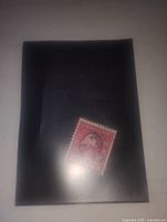 Photo of a vintage 2 cent George Washington postage stamp mounted on a black holder, showing the front design and color.