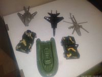 Top-down view showing 3 planes (stealth bomber, jet fighter, fighter plane), 1 military helicopter, 2 camouflaged jeeps, and 1 inflatable boat on white background.