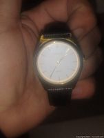Photo of vintage Cardinal wristwatch showing the white dial with gold-tone markers and black leather strap held in the hand.