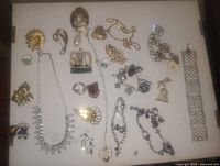 Overhead photo showing a broad assortment of vintage costume jewelry pieces, including necklaces, brooches, bracelets, rings, and pendants arranged on a white surface.