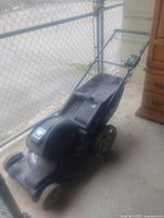 Full view of black electric lawnmower with grass bag and handle in used condition.