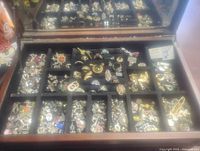 Top compartment view showing multiple divided sections filled with assorted fashion rings and brooches in a black felt-lined tray