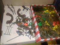 View of plastic army men and accessory toys scattered inside and outside a checkered metal tin.