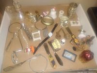Top-down photo of various small used items in a box including glass jars, bracelets, watches, magnifying glasses, small figurines and miscellaneous trinkets.
