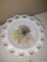 White milk glass candy bowl with scalloped and pierced edge holding seven small Wade England porcelain figurines of various designs and colors.