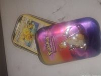 Photo shows an open Pokémon tin featuring Dragonite on the lid and several Pokémon cards inside, including a Seel card on top.
