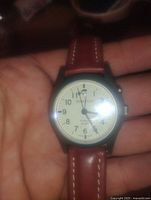 Front view of Momentum men's wrist watch showing white dial, black numerals, red leather band, and glow in the dark hands.