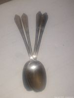 Photo showing four antique silver plated spoons with detailed handles and oval bowls laid out on a white background.